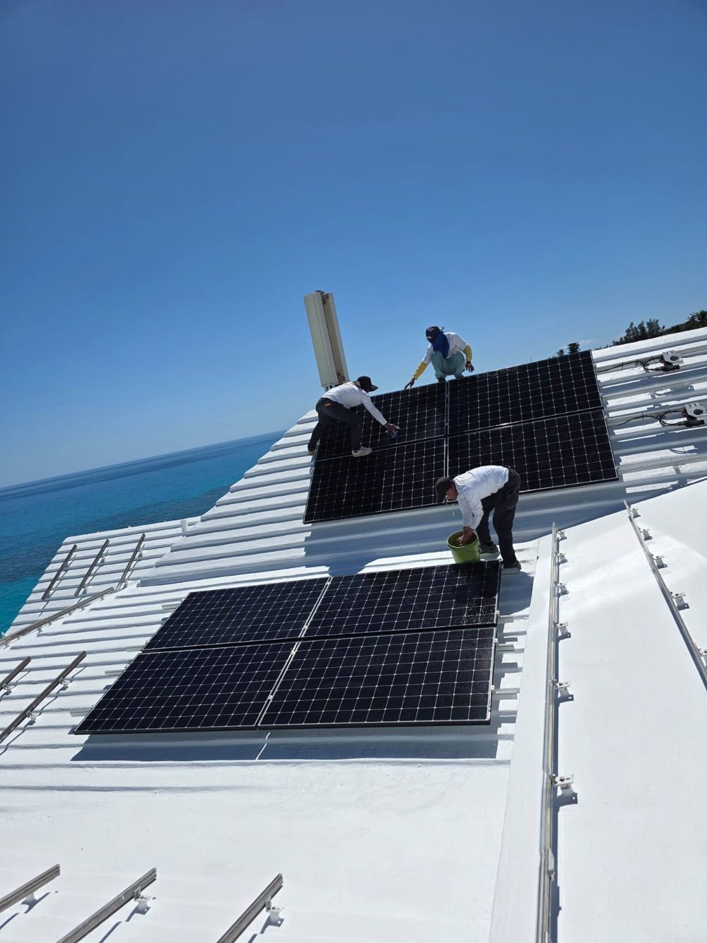 The crew reinstalling solar panels on a freshly coated roof above the sea